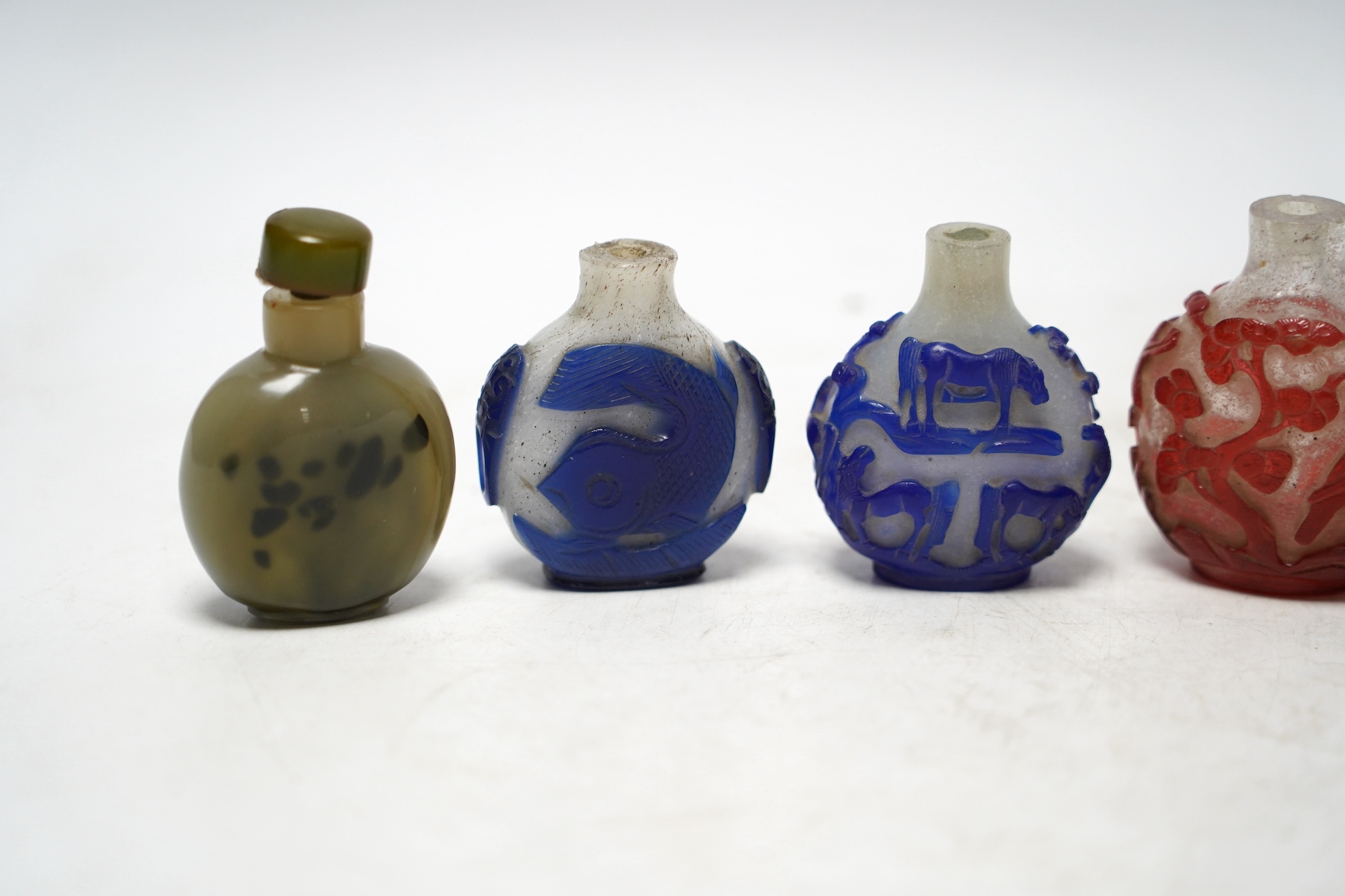 A Chinese moulded and white glazed ‘Buddhist lion’ snuff bottle, 19th century and three overlaid glass snuff bottles 6.5cm high (4)
